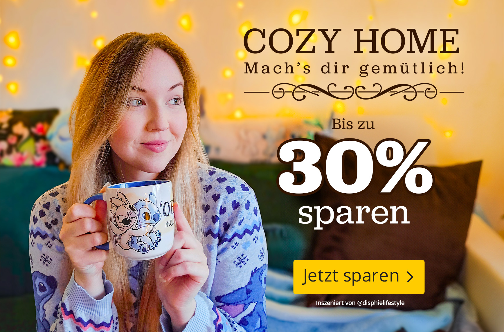 Gemütliche Wohnszene mit einer Frau im Lilo & Stitch Pyjama, die eine Stitch Tasse hält. Hintergrund mit warmen Lichterketten. Text: Cozy Home, Mach’s dir gemütlich, bis zu 30 Prozent sparen, Jetzt sparen.