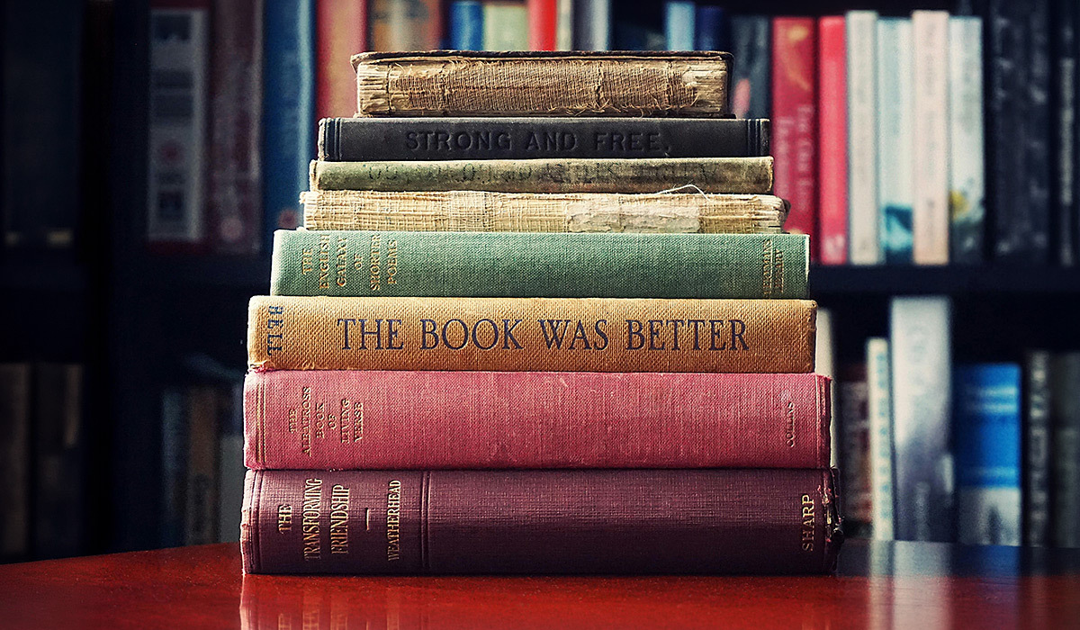 Stacked books on a table. The background shows a bookshelf.