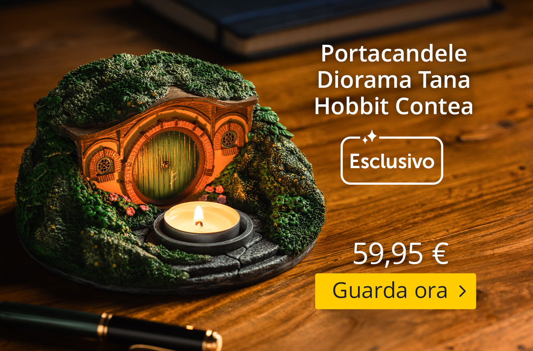 Portacandela dettagliato a forma di tana degli Hobbit della Contea, con porta rotonda verde, muschio e fiori su un tavolo di legno. Testo: “Tana Hobbit Diorama Portacandela, Esclusivo, 59,95 €, Guarda ora”.