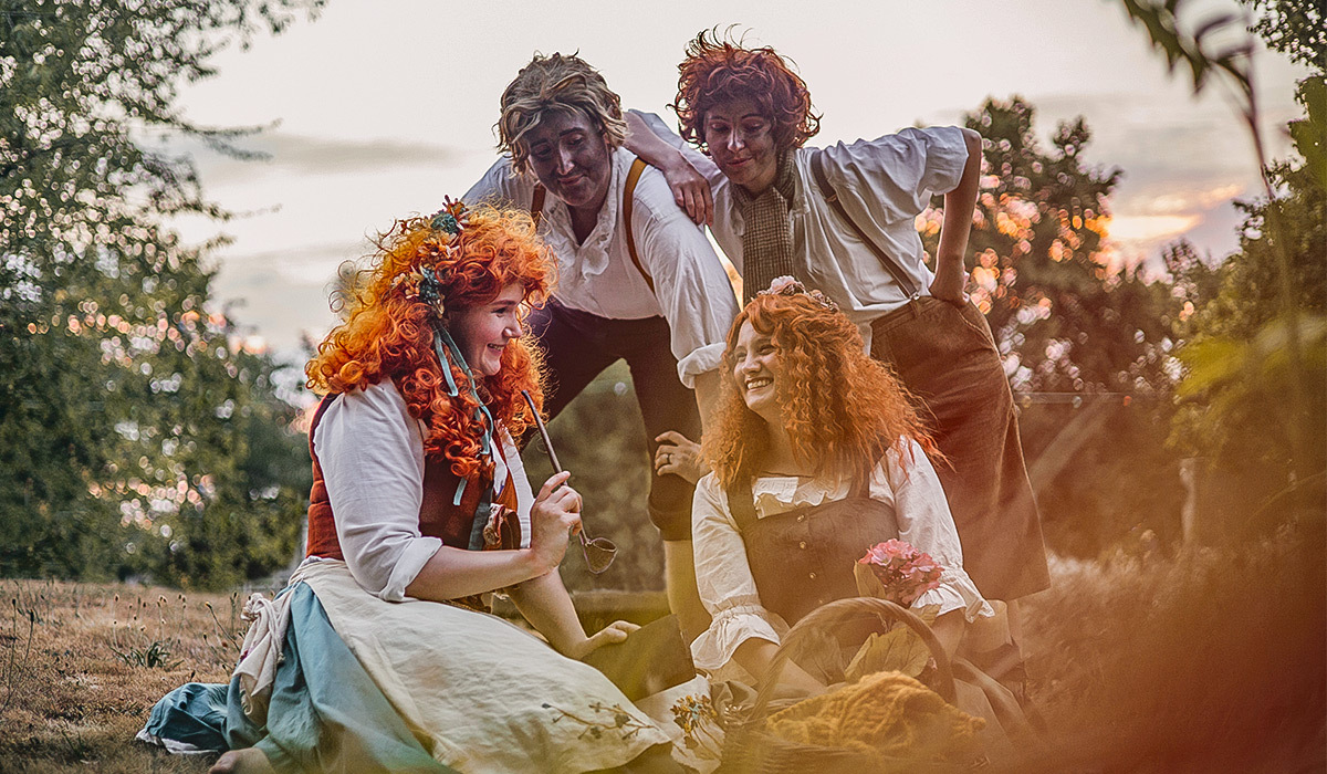 Quattro persone in cosplay de “Il Signore degli Anelli” posano da hobbit in un giardino al tramonto, con abiti rustici, parrucche ricce e un cesto da picnic.