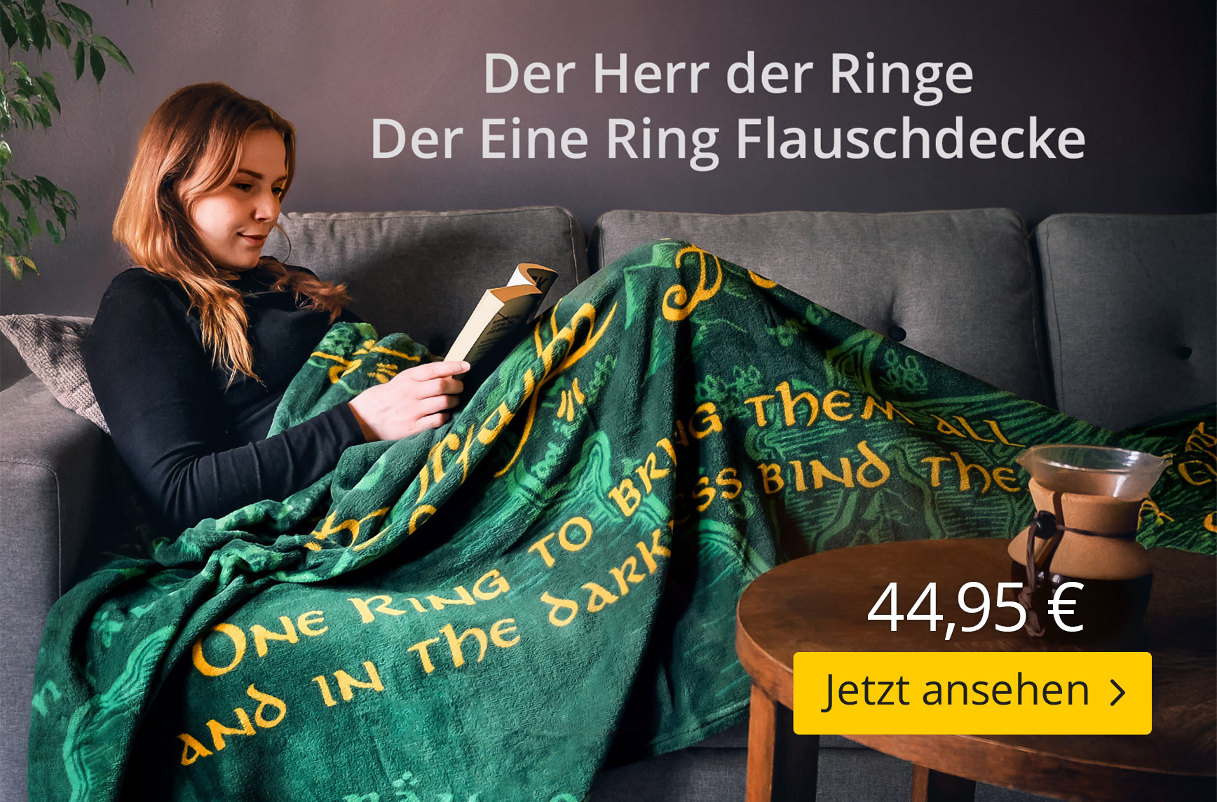 Frau liest auf dem Sofa und ist in eine grüne Flauschdecke mit goldgelber Inschrift aus Der Herr der Ringe gehüllt. Text: Der Herr der Ringe – Der Eine Ring Flauschdecke – 44,95 € – Jetzt ansehen. Elbenwald-Produktgrafik.