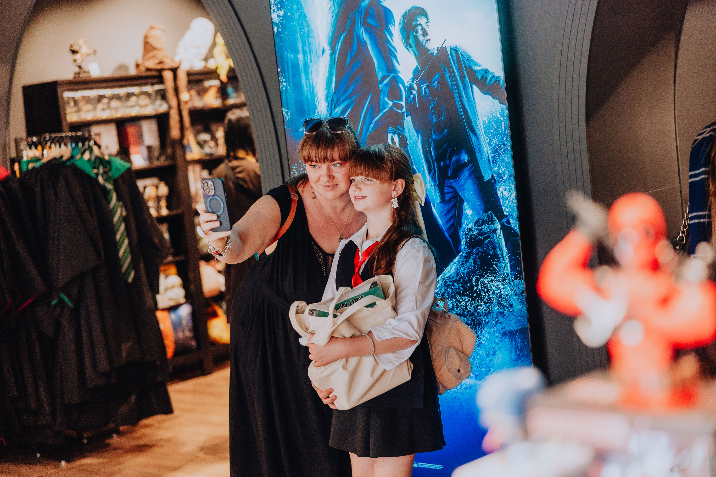 Two customers take a selfie in an Elbenwald store in front of a glowing Harry Potter sign.