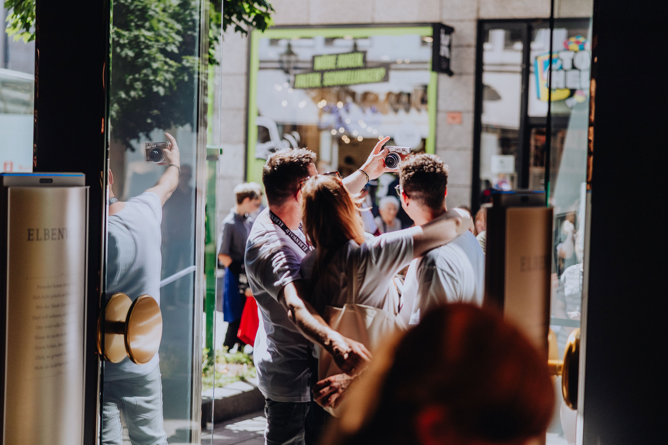 Three Elbenwald employees take a selfie with an instant camera in front of the store.