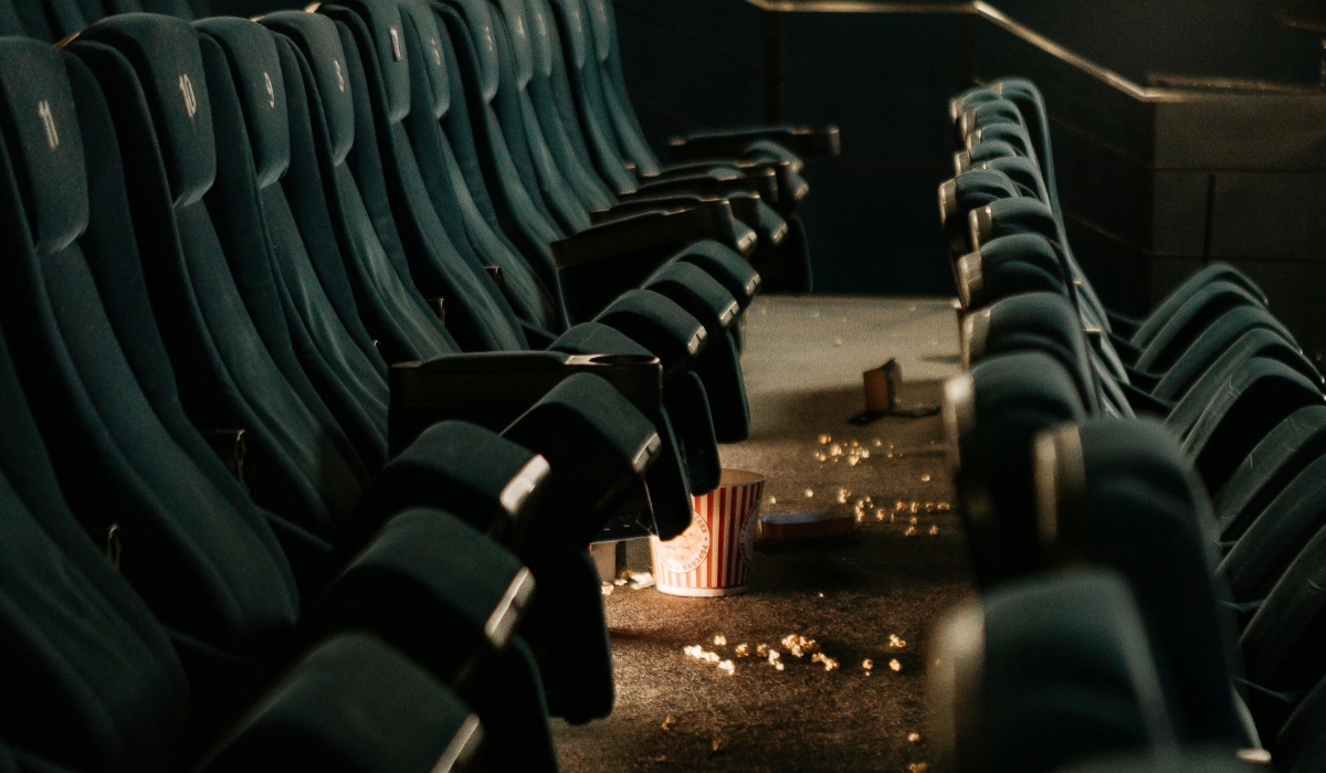 Row of empty cinema seats with spilled popcorn and a tipped-over popcorn bucket on the floor. Warm light falls across the scene, evoking the end of a movie screening. Text: Pure cinema vibes – time for another Marvel marathon.
