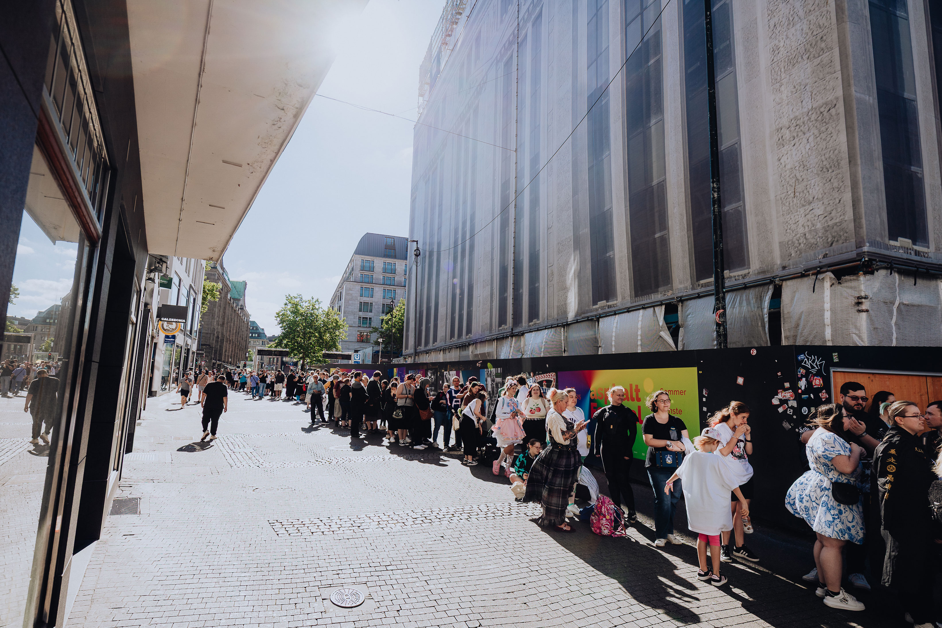 A long queue of people waits in bright sunshine for the new Elbenwald store to open.