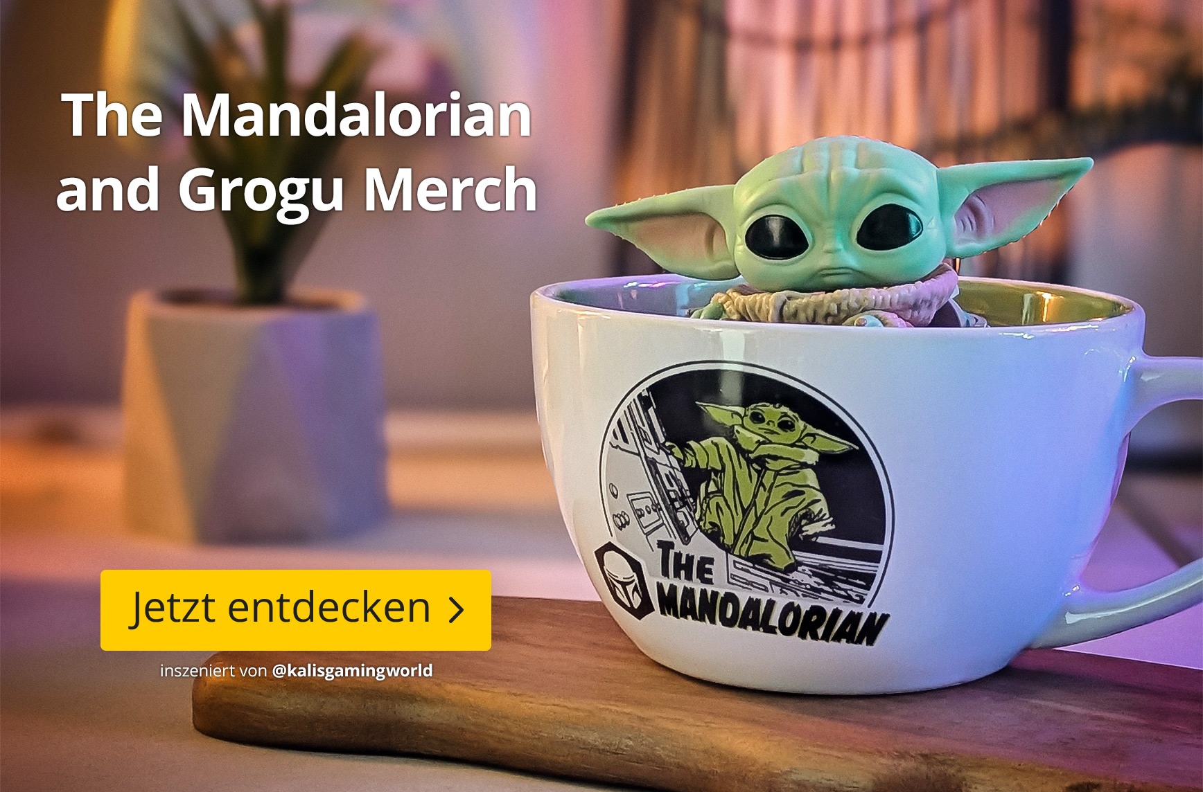 Grogu aus The Mandalorian sitzt in einer großen weißen Tasse mit Mandalorian-Motiv auf einem Holztisch. Im Hintergrund stehen eine Zimmerpflanze und warme Lichter. Text: The Mandalorian and Grogu Merch, Jetzt entdecken.