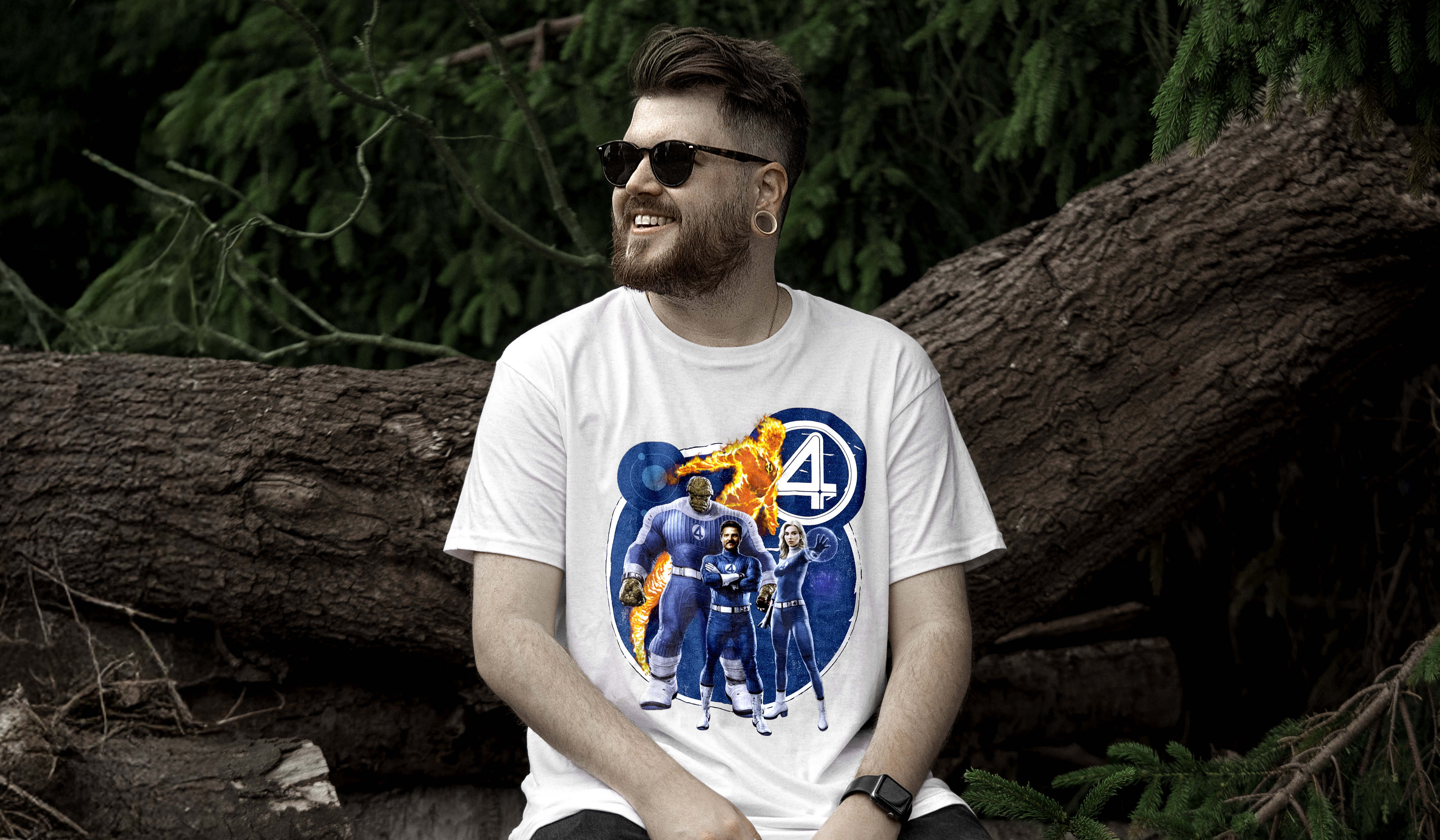 Mann mit Bart und Sonnenbrille trägt ein weißes Fantastic-Four-T-Shirt mit Comic-Motiven. Im Hintergrund: umgestürzte Bäume und grüne Waldkulisse.