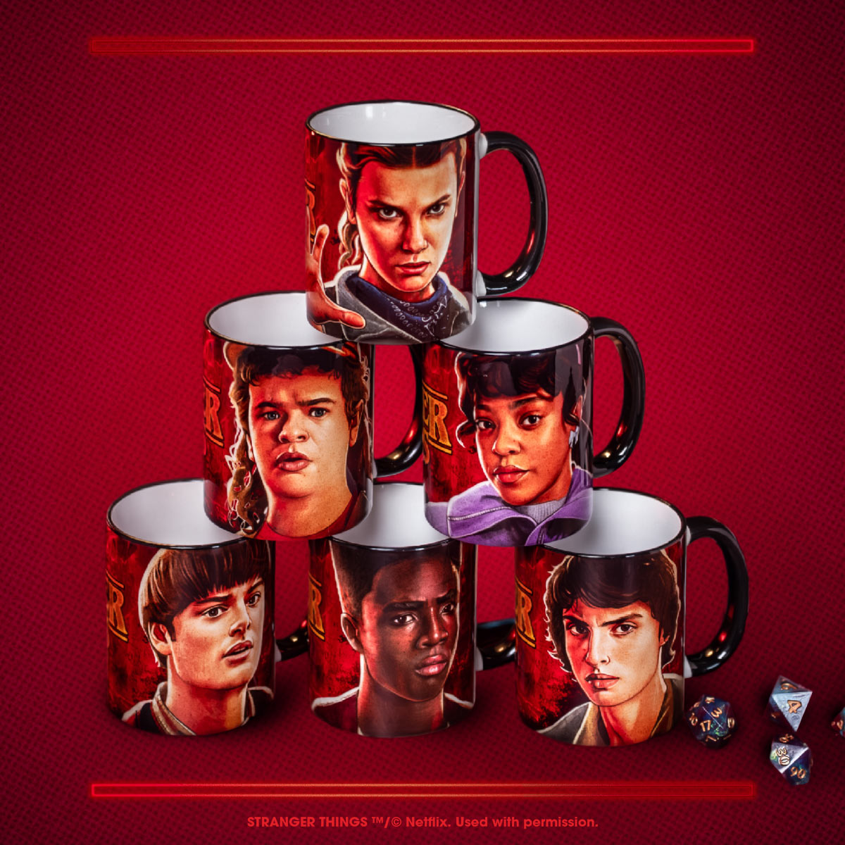 Pyramide aus sechs Stranger-Things-Tassen mit Porträts der Figuren Eleven, Dustin, Erica, Will, Lucas und Mike auf rotem Hintergrund. Daneben liegen einige mehrfarbige Würfel.