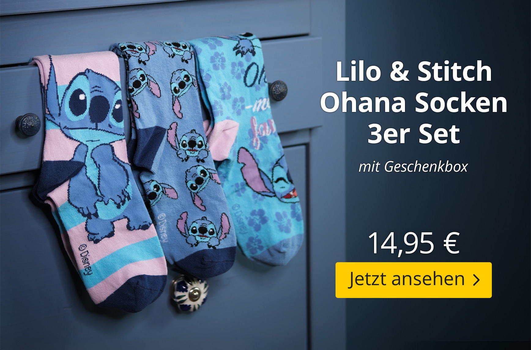 Drei Paar Lilo & Stitch Socken aus einem Geschenkset hängen an einer blauen Kommode. Die Motive zeigen Stitch in verschiedenen Designs und Farben. Lilo & Stitch Ohana Socken 3er Set mit Geschenkbox, 14,95 €, Jetzt ansehen.