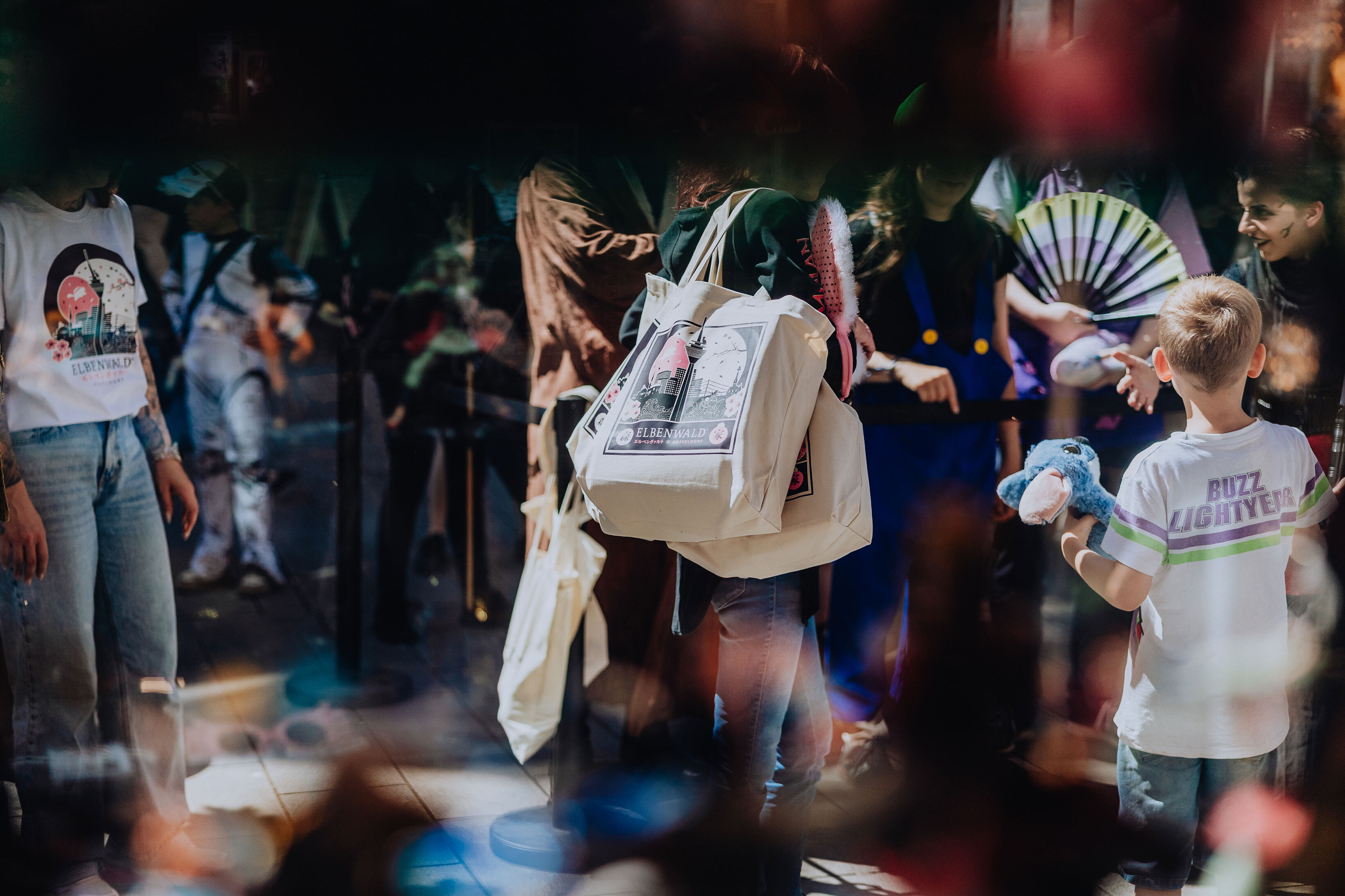 Customer carrying several Elbenwald tote bags stands in front of the store. She is surrounded by other people waiting, though they appear blurred.